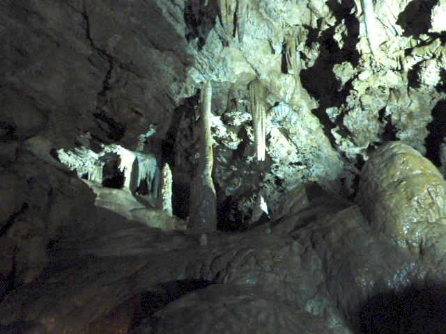 Interior of a cave featuring stalactites and stalagmites, illuminated by soft light.