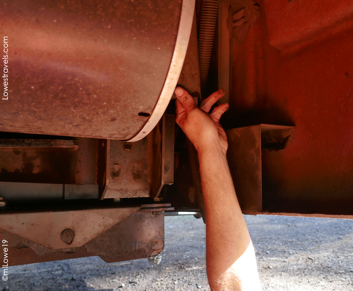 A person reaching under a truck to make adjustments, with tools visible near their hand.