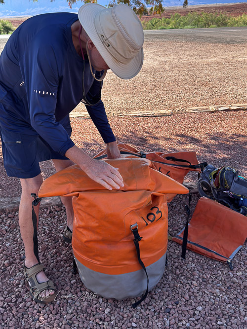A person securing an orange dry bag, preparing for a river rafting trip.