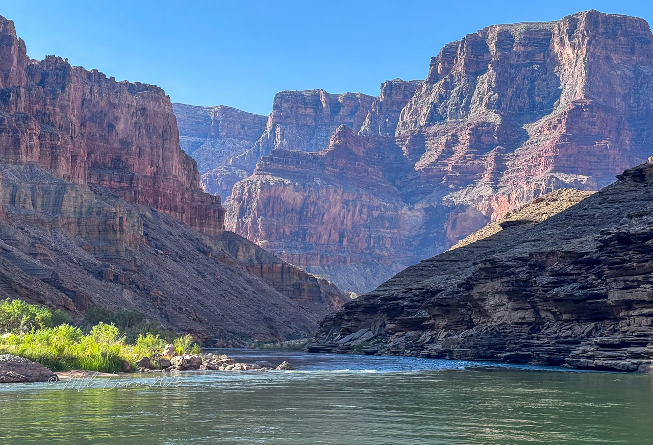 Scenic view of the Colorado River winding through the Grand Canyon, with towering red rock formations and clear blue skies above.