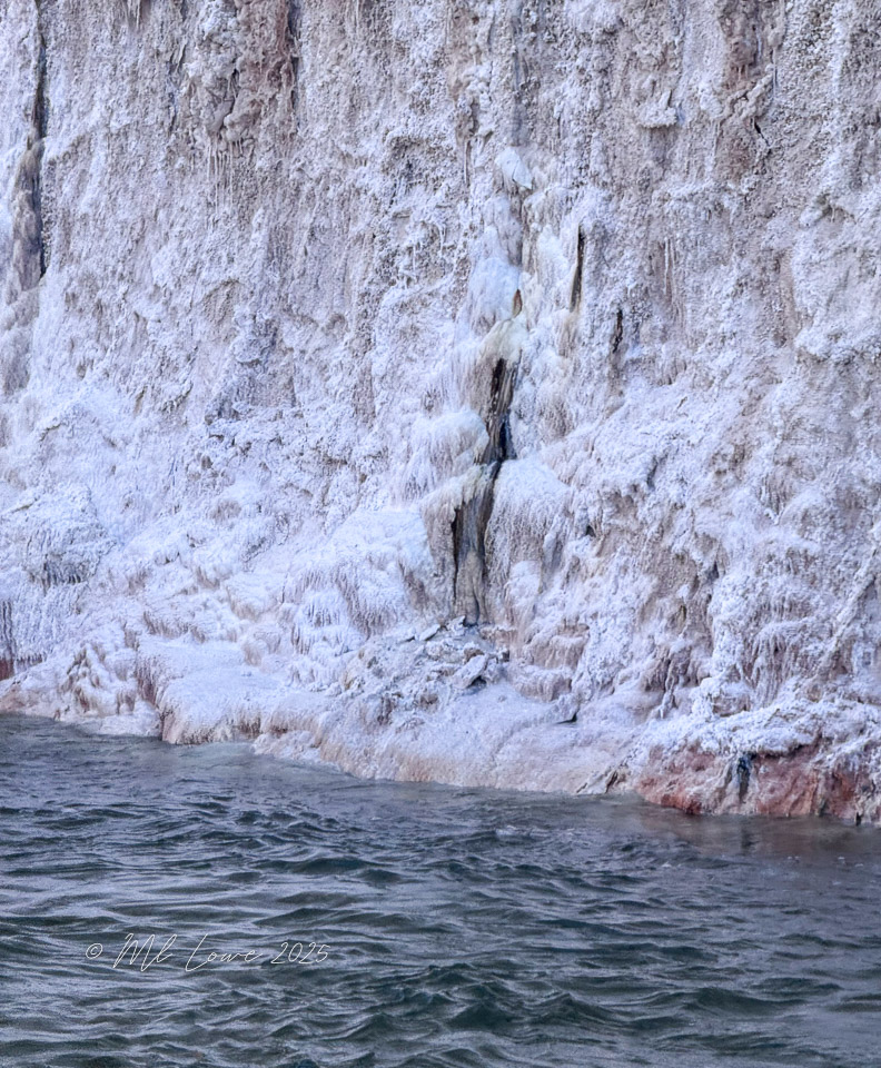 Close-up view of a rocky canyon wall with a textured surface, partially covered in white mineral deposits, above the calm waters of the Colorado River.