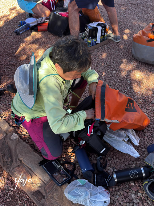 Person preparing gear and packing supplies ahead of a river rafting trip at the Grand Canyon, sitting on rocky ground.