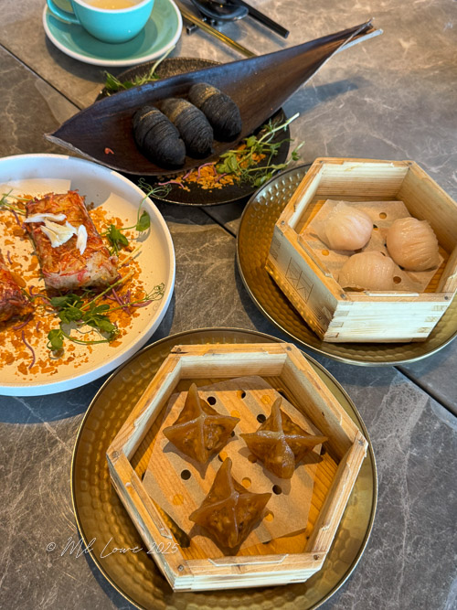 A table setting featuring various types of Dim Sum, including steamed dumplings in bamboo baskets, a plate of crispy seafood dish, and uniquely shaped savory pastries.