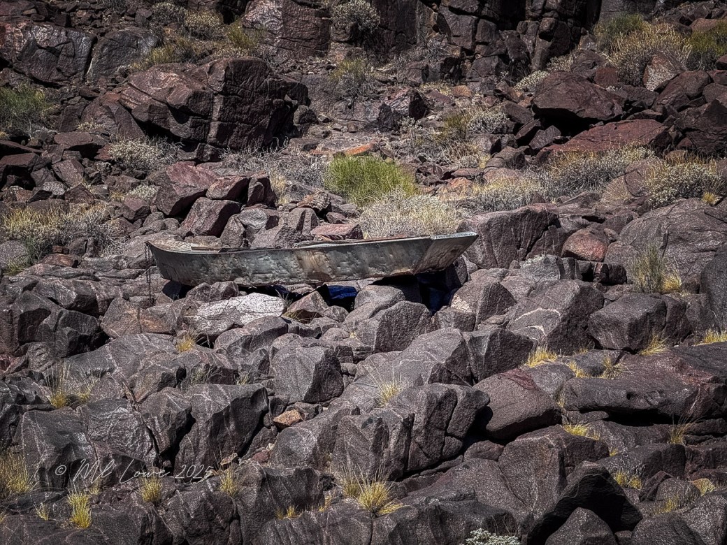 An old, weathered metal boat rests on a rocky terrain surrounded by sparse vegetation in the Grand Canyon.