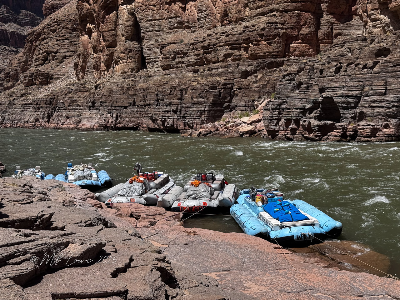 Rafts anchored along the Colorado River with rocky canyon walls in the background, showcasing the scenic landscape of the Grand Canyon.