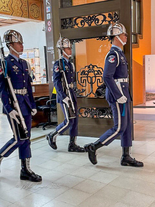 Three soldiers in formal uniforms with helmets march in a hallway, showcasing a ceremonial display.