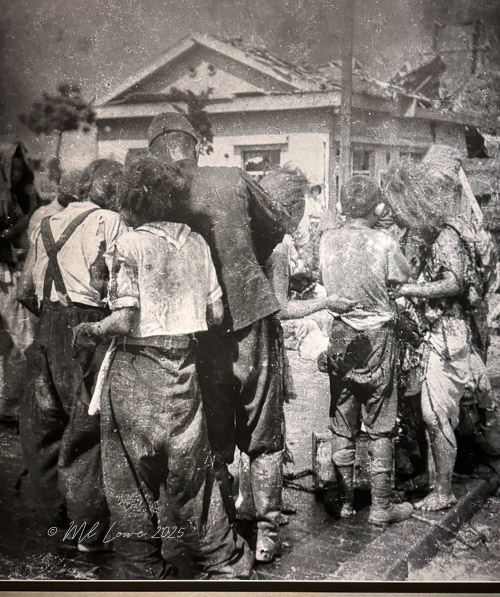 A historical black-and-white photograph depicting a group of survivors in a post-war scene, showcasing their injuries and struggles in the aftermath of the Hiroshima atomic bombing.