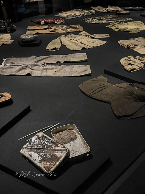 A display of personal items and clothing remnants from Hiroshima atomic bombing victims, shown on a black background.