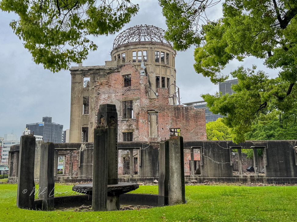 The Hiroshima Peace Memorial, an iconic structure with a partially collapsed dome, surrounded by greenery and modern buildings in the background.