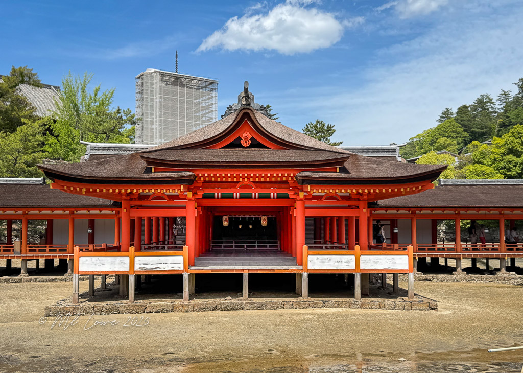 A view of the Itsukushima Shrine, showcasing its iconic red architecture standing on stilts over the water, with a clear sky in the background.