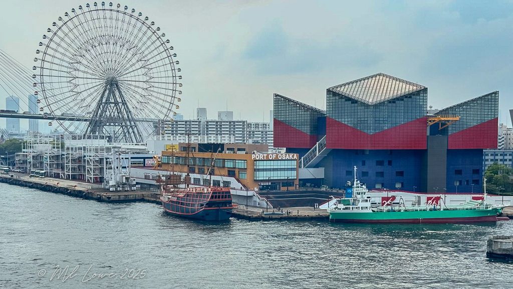 View of Osaka port featuring a large ferris wheel, a historical ship, and modern buildings along the waterfront.