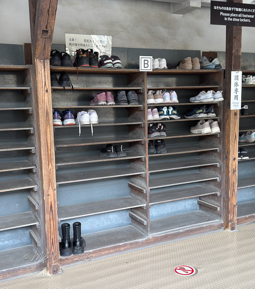 Shoe storage area with various pairs of shoes neatly organized on wooden shelves, indicating a cultural practice of removing shoes before entering certain spaces.
