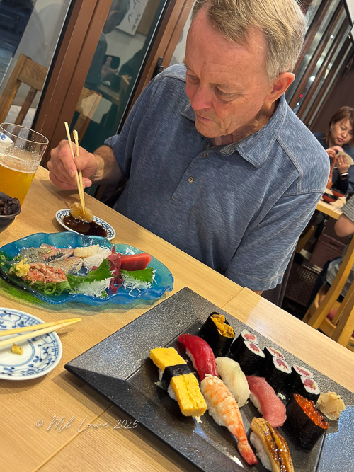 A man enjoying a sushi meal at a restaurant, with a plate of sashimi and assorted sushi in front of him.