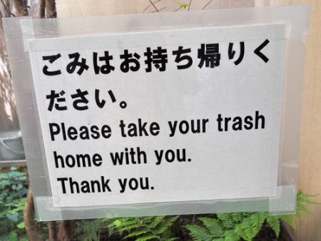 A sign instructing visitors to take their trash home, written in Japanese and English, surrounded by ferns.