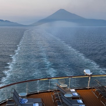 View of Mount Fuji in the distance from a cruise ship deck, with the ocean in the foreground and chairs arranged for relaxation.