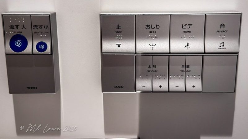A close-up image of a modern toilet control panel featuring buttons for flushing, bidet functions, pressure, volume, and privacy options, labeled in Japanese and English.