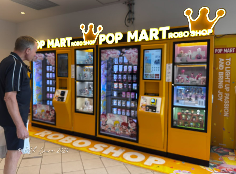 A man stands in front of a brightly lit vending machine shop called 'POP MART ROBO SHOP' featuring various collectible figures and toys.