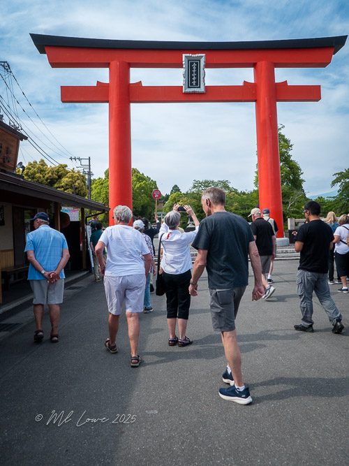 Visitors walking towards a large red torii gate, a traditional Japanese gate, on a street lined with shops.