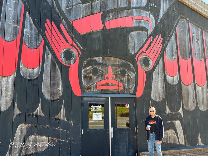 A person standing in front of a large wooden wall decorated with a red and black indigenous art mural, with a door labeled 'CLOSED' nearby.