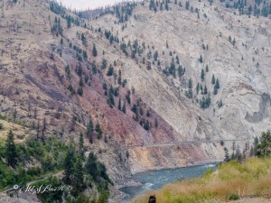 A scenic view of colorful mountainsides with sparse trees and a river winding through the valley below.