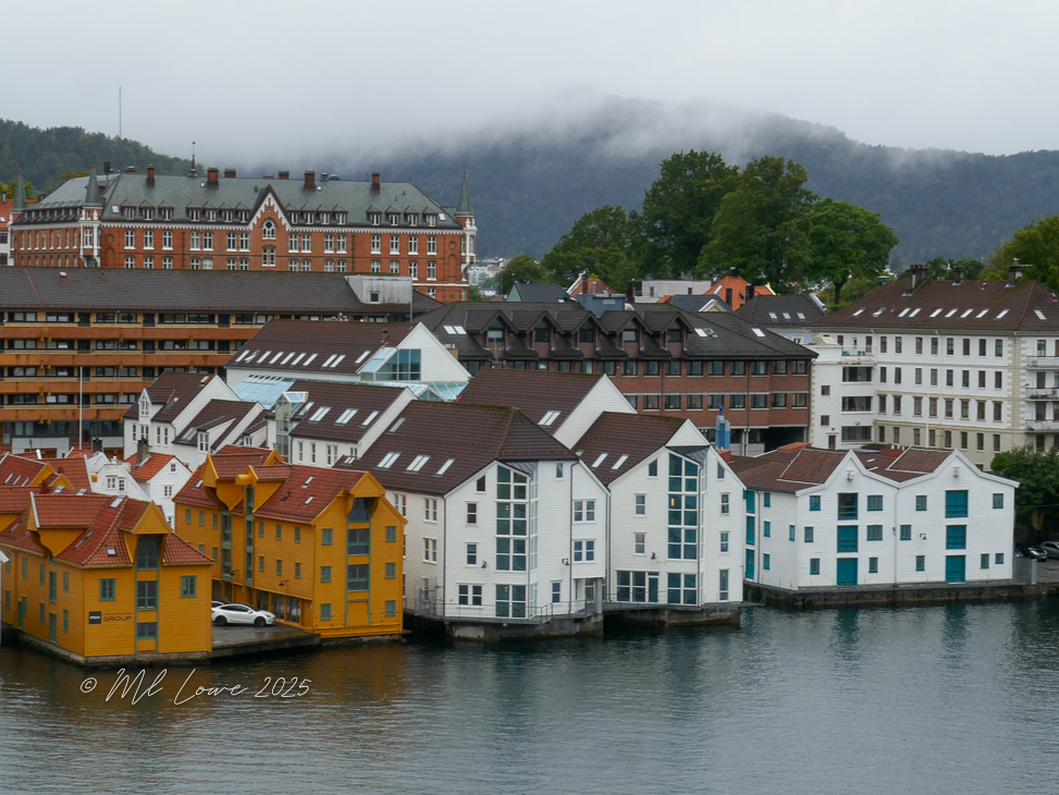 View of colorful architecture along the waterfront in Bergen, Norway, featuring a mix of modern and traditional buildings under a cloudy sky.