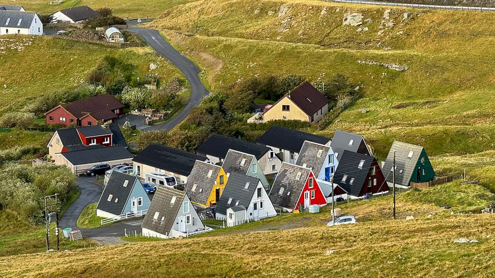 A colorful cluster of houses nestled in a green landscape, with a winding road nearby.