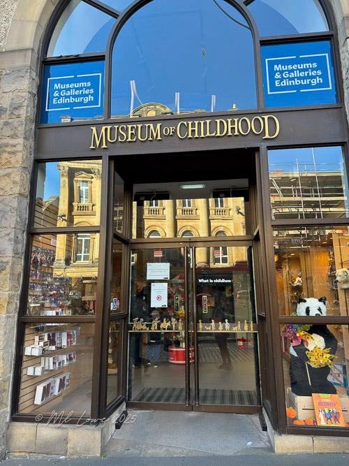 Entrance to the Museum of Childhood in Edinburgh, featuring large glass doors with the museum's name prominently displayed above.