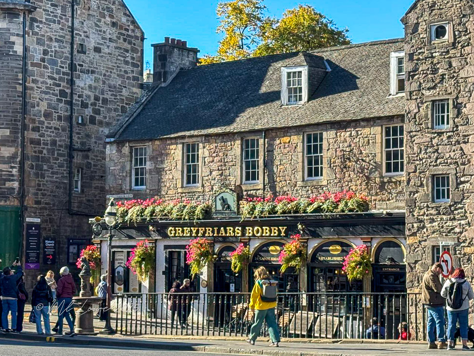 Exterior view of Greyfriars Bobby pub in Edinburgh, adorned with flowers and featuring historical architecture.