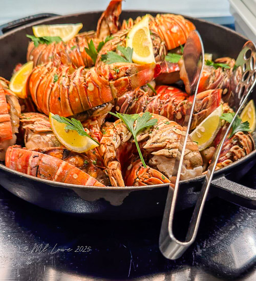 A skillet filled with freshly cooked lobsters garnished with lemon slices and parsley.
