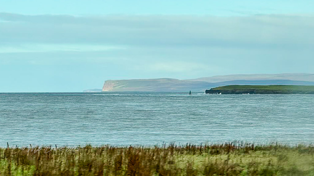 View of the coastline near John o' Groats, with a cloudy sky and grass in the foreground.