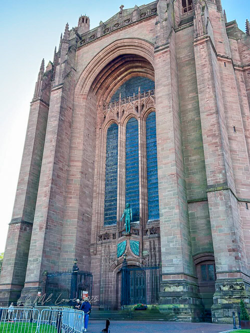 Exterior view of a large cathedral with intricate stonework and tall stained glass windows, featuring a statue at the entrance.