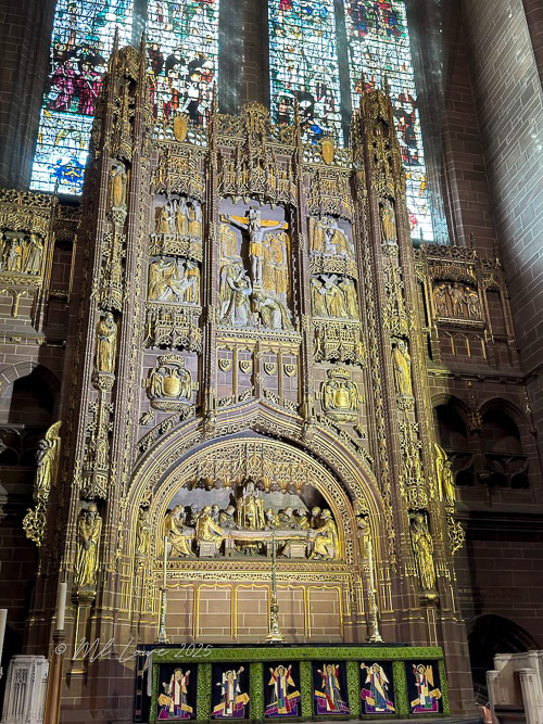 A beautifully detailed altarpiece featuring intricate carvings and religious scenes, set against the backdrop of stained glass windows in a cathedral.
