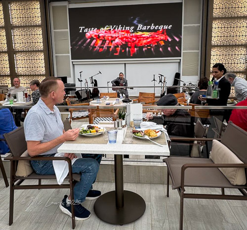 A man enjoys a meal during the 'Taste of Viking Barbeque' event, with live music in the background and other diners seated at tables.