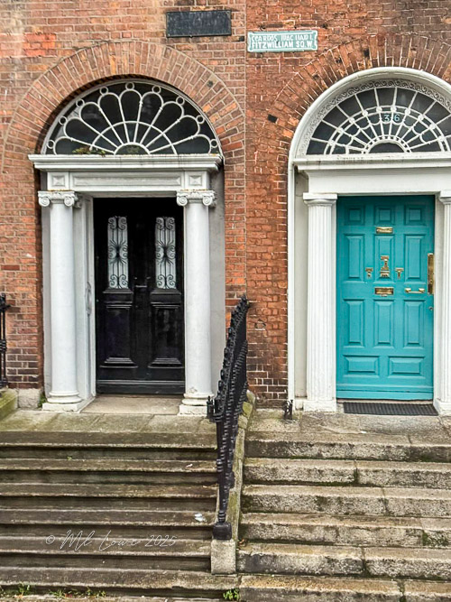 Close-up of two Georgian-style front doors in Dublin, one black and the other turquoise, featuring decorative elements and stairs.
