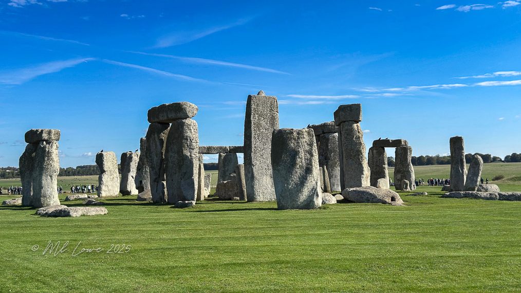 Stonehenge, a prehistoric monument of large standing stones, set in a green landscape under a blue sky.