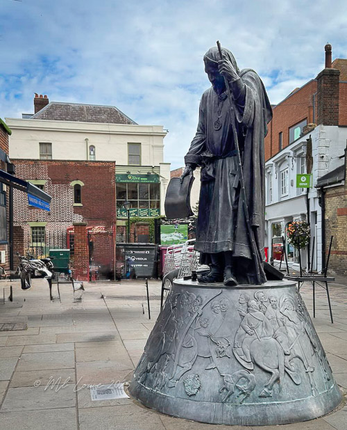 Statue of a Viking figure in a historical setting, surrounded by buildings and shops.