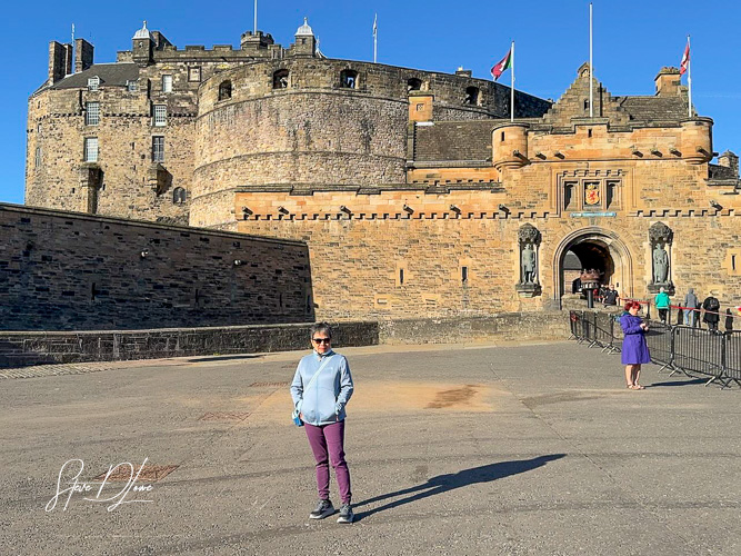 A person standing in front of Edinburgh Castle, showcasing the iconic stone structure and a clear blue sky in the background.