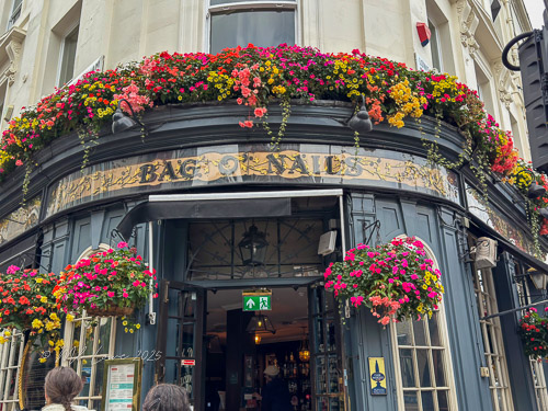 Exterior of the Bag of Nails pub in London, adorned with colorful flowers and greenery.