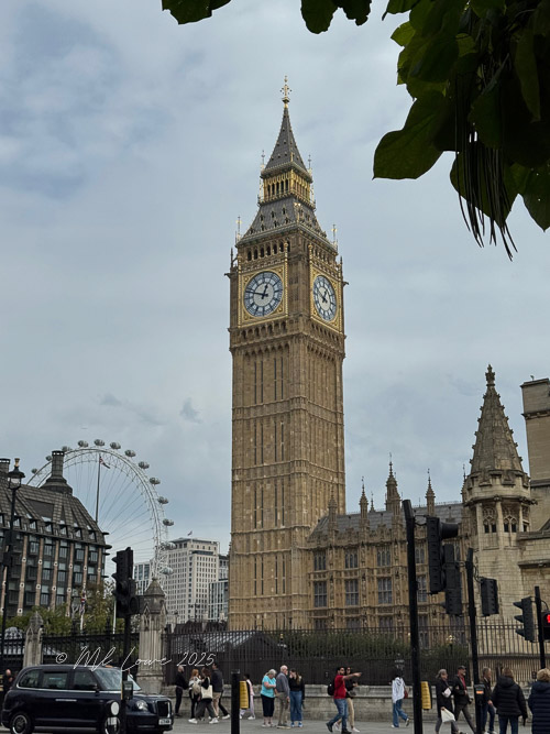 A close-up view of Big Ben, the iconic clock tower in London, showcasing its intricate architecture and clock face, with the London Eye visible in the background under a cloudy sky.