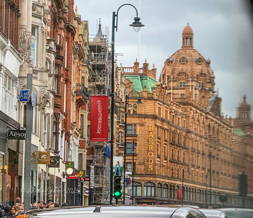 A street view of Knightsbridge in London, showcasing the iconic Harrods department store with its distinctive architecture, surrounded by urban streets and shops.