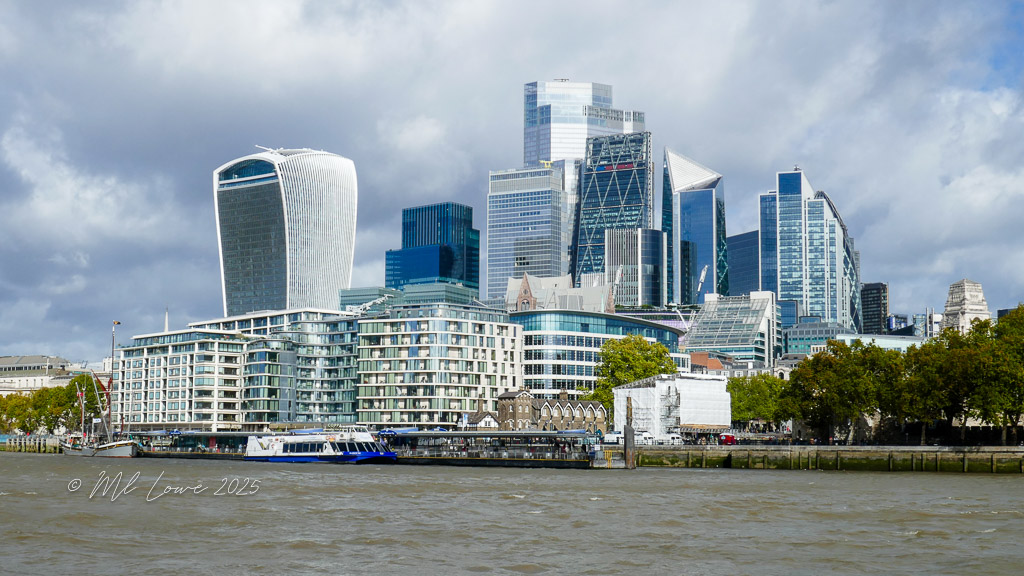 A view of London's modern skyline featuring iconic skyscrapers and buildings along the River Thames under a partly cloudy sky.