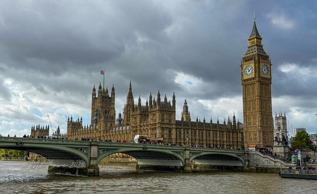 View of the iconic Parliament Building and Big Ben in London, taken from across the River Thames under a cloudy sky.