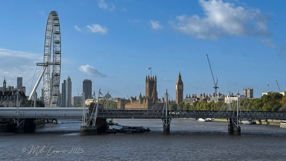 View of the London Eye and the Houses of Parliament across the River Thames under a blue sky.