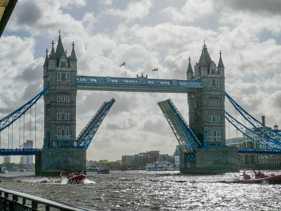 Tower Bridge in London with one of its drawbridges raised, allowing a boat to pass underneath, surrounded by a cloudy sky.