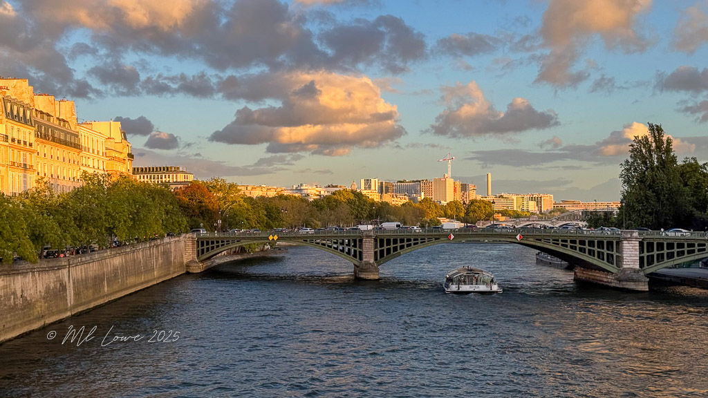 A scenic view of the River Seine in Paris during sunset, showcasing a bridge with a boat passing underneath and buildings lined along the riverbank.