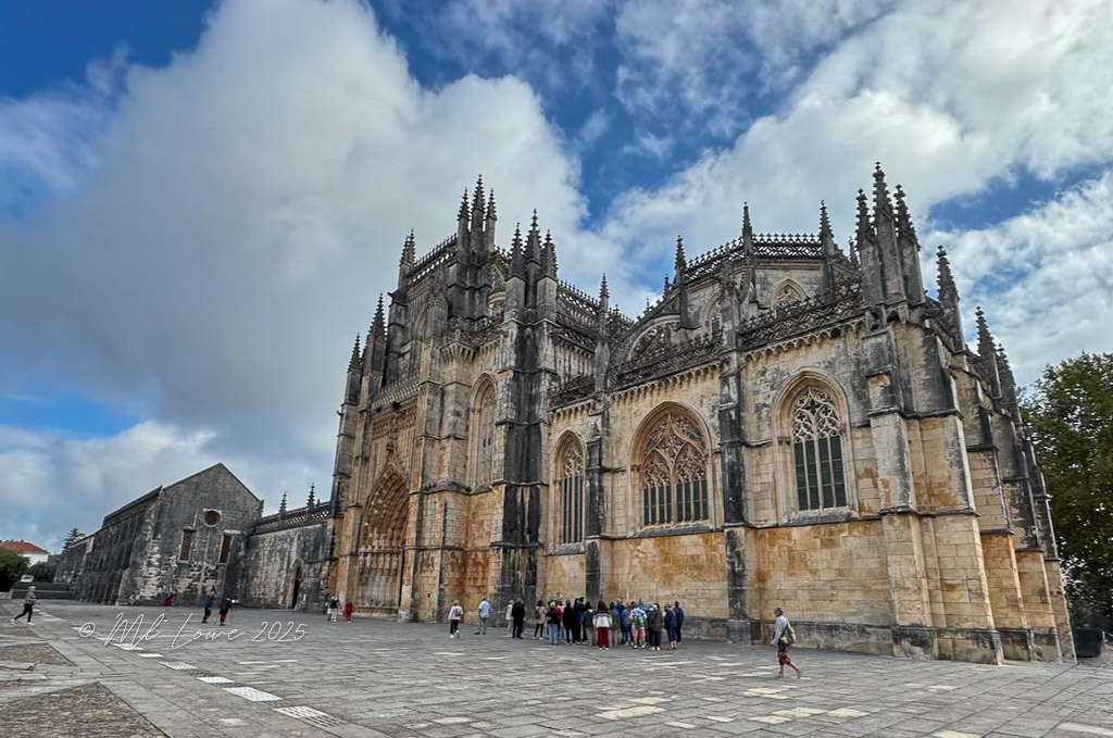 The exterior of the Batalha Monastery in Portugal, showcasing its intricately designed Gothic architecture and spires against a blue sky.