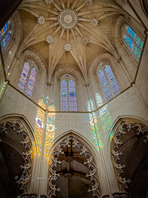 Interior view of a gothic-style church featuring ornate architecture with a star-shaped ceiling and stained glass windows casting colorful reflections on the stone walls.