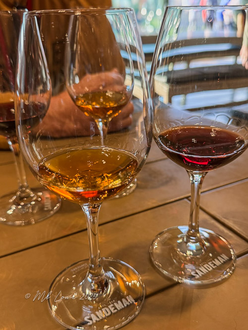 Three glasses of port wine in varying shades, with a hand visible in the background, indicating a tasting experience.