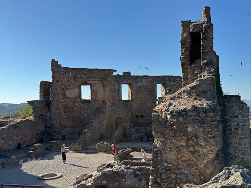Ruins of a historical stone fortress with people exploring the site on a sunny day.