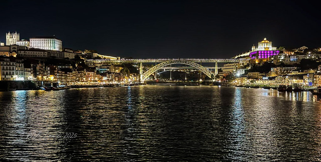 Night view of the illuminated Porto skyline, featuring the Dom Luís I Bridge over the Douro River, surrounded by well-lit buildings along the waterfront.